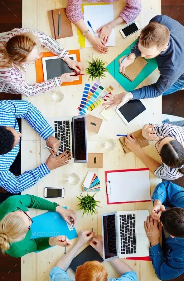 Overhead view of colleagues at a table with laptops, tablets, phones, and notebooks