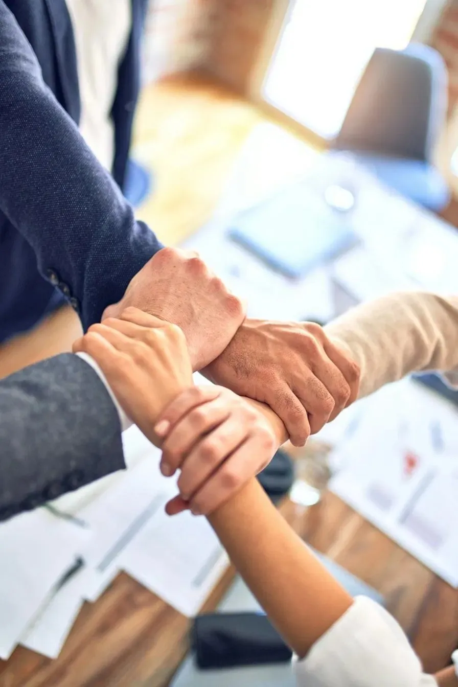 Colleagues clasping each other's wrists in a circle over a desk, showing teamwork